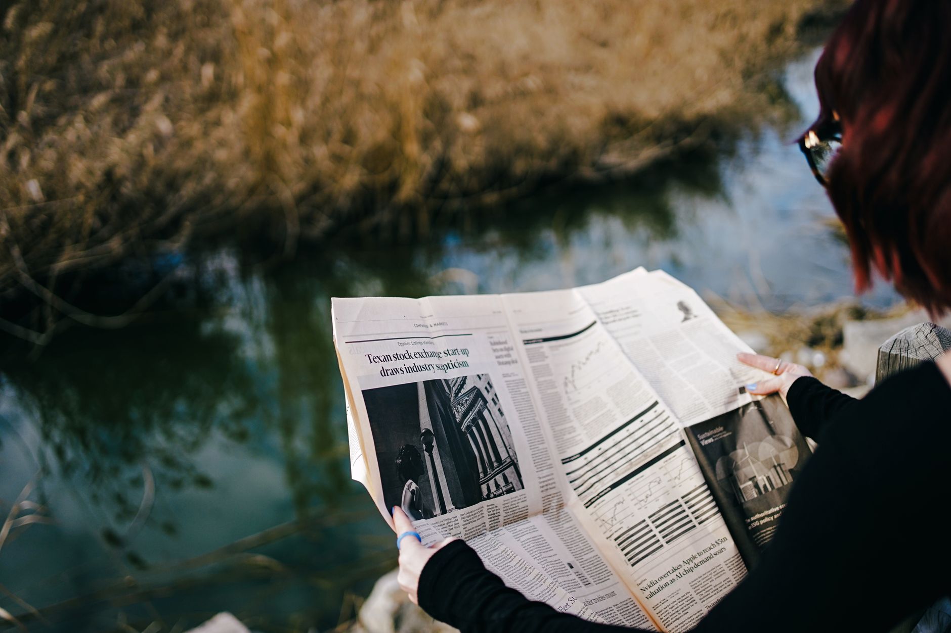 A person enjoys reading a newspaper by a tranquil pond on a sunny day. — examplearticle